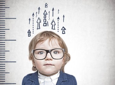 Mavi takım ve gözlük bir cetvel ve onu çizilmiş gösteren oklar ile beton duvarının yakınında duran sevimli küçük çocuk. Büyüme kavramı