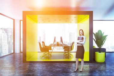 Uzun ahşap bilgisayar tablo siyah ve ahşap sandalye ve gri kanepeli lobide duran sarı ve ahşap açık alan ofiste iş kadını. Tonlu görüntü