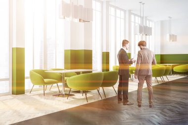 İşadamları beyaz ve yeşil duvarlar, ahşap zemin, çatı windows ve yeşil koltuklar ile ahşap masa ile modern kafe köşesinde. Tonlu görüntü