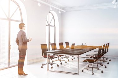 İşadamı toplantı salonu ile beyaz duvarları, kiremitli kat, kemerli windows ve siyah sandalye ile uzun, siyah ahşap masa ofis köşesinde. Tonlu görüntü