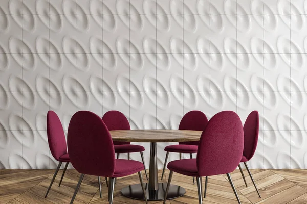 Interior of modern dining room with white geometric wall pattern, wooden floor and round wooden table with red chairs standing around it. 3d rendering