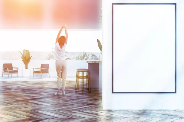 妇女站在现代化的厨房与白色的墙壁 木地板 灰色和木制酒吧与凳子和扶手椅在阳台上 墙上的垂直海报 色调图像模拟 — 图库照片