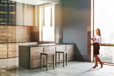 Kadın beyaz ve tuğla duvarlar, modern mutfak köşesinde döşeli zemin, gri ve ahşap mutfak tezgahı ve gri ve ahşap bar tabureleri ile. Çift tonlu görüntü pozlaması