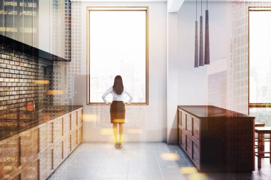 Beyaz ve siyah tuğla duvarlar, kiremitli kat, gri ve ahşap mutfak tezgahı ve gri ile modern mutfak yan görünüm ve ahşap bar tabureleri ile. Kadının yanına pencere. Çift tonlu görüntü pozlaması