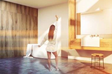 Kadın beyaz ve ahşap duvarlar, beton zemin, beyaz küvet ve ahşap tezgah üzerinde duran lavabo banyo köşesinde. Tonlu görüntü