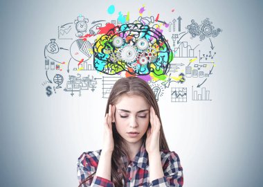 Kareli gömlek giymiş ve dişliler ve iş ikonları/simgeleri ile renkli beyin kroki ile gri duvarının yakınında oturan bir baş ağrısı olan stresli genç kadın portresi