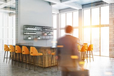 Adam beyaz duvarlar, beton zemin, büyük pencereler, yanında duran sarı dışkı ile ahşap ve gri bar ile modern bar köşesinde. Raflar şarapları. Çift tonlu görüntü pozlaması bulanıklık