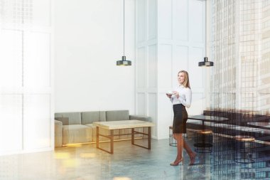 Kadın beyaz duvarlar, beton zemin, uzun gri kanepe yuvarlak siyah tablolar ve ahşap sandalye ve ahşap masa yakınındaki gri kanepe yakın duran modern kafe köşesinde. Çift tonlu görüntü pozlaması