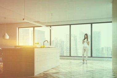 Beyaz duvarları, ahşap zemin, panoramik pencere ve beyaz ada ile modern mutfak iç kadında inşa tencere ve lavabo. Çift tonlu görüntü pozlaması