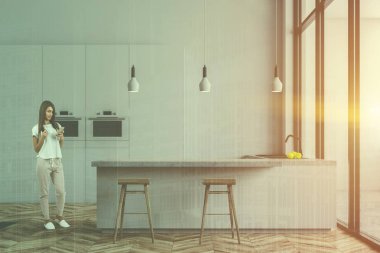 Beyaz duvarları, ahşap zemin, çatı windows ile minimalist beyaz mutfak kadında, fırınlar ve tezgah lavabo ile yanındaki dışkı ile beyaz çubuğu ile beyaz dolap inşa. Çift tonlu görüntü pozlaması