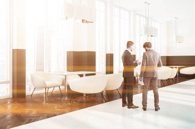 İşadamları beyaz ve kahverengi duvarlar, ahşap zemin, çatı windows ve beyaz koltuklar ile ahşap masa ile modern kafe köşesinde. Tonlu görüntü