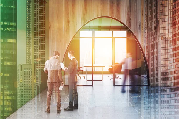 Men near manager office with green and wooden walls, large window, desk with laptop, manager chair and two visitors chairs as seen through arched door in the lobby. Toned image double exposure blur