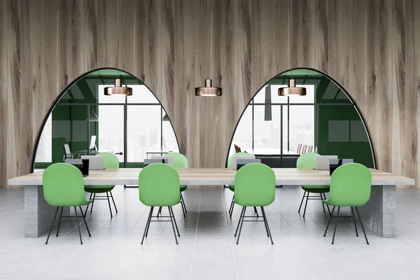 Interior of modern office with green and wooden walls, tiled floor, long wooden and stone table with laptops on it and green chairs. Manager office and meeting room seen through windows. 3d rendering