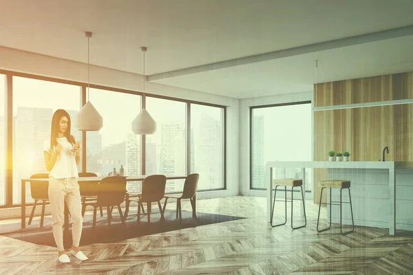 Kadın beyaz ve ahşap duvarlar, ahşap zemin, beyaz ada ve dışkı ile ve sandalye ile gri barıyla modern mutfak köşesinde. Çift tonlu görüntü pozlaması