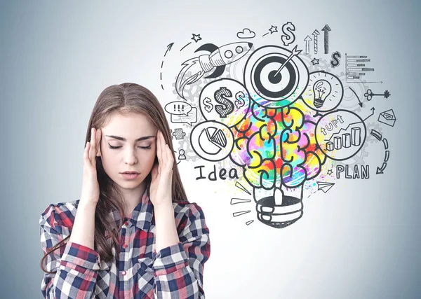 Kareli gömlek giymiş ve renkli iş fikir kroki ile gri duvara yakın oturan bir baş ağrısı olan stresli genç kadın portresi