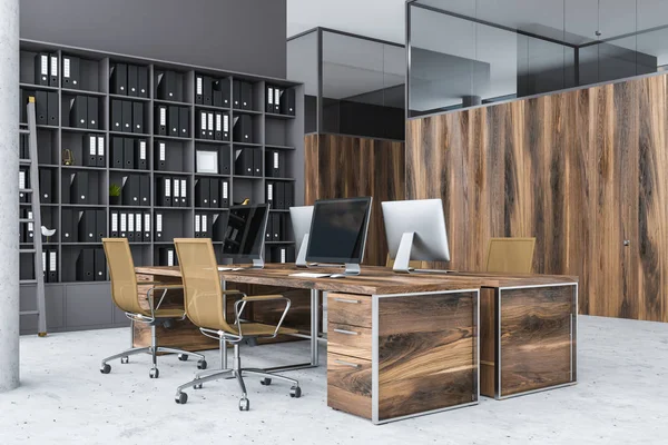 Corner of gray office with wooden computer tables with brown chairs, a bookcase with folders and wooden office doors. 3d rendering