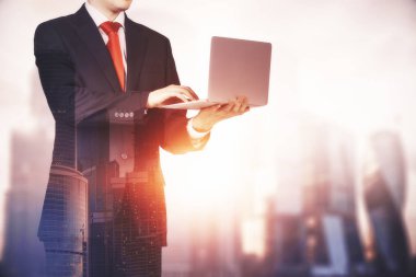 Takım ve kırmızı kravat ve bulanık cityscape arka plan üzerinde laptop ayakta tutan tanınmayan bir işadamı. Çift tonlu görüntü pozlaması