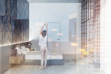 Beyaz ve ahşap duvarlar, ahşap zemin, gri karyola ve beyaz ve cam kapı ile yatak odası iç yan görünüm. Kadın pijama. Çift tonlu görüntü pozlaması