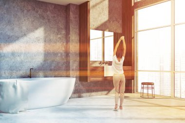 Beton duvarlar, beyaz zemin, Banyo köşesinde kadında çatı penceresi, beyaz küvet ve ahşap tezgah üzerinde duran lavabo. Tonlu görüntü