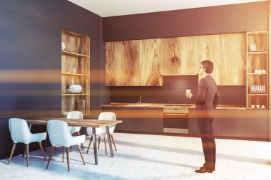 Gri duvarlar, beton zemin, gri mutfak tezgahı ve ahşap dolapları ve büyük gri ve ahşap dolap modern mutfak köşe soldaki adam. Ahşap masa sandalye ile. Tonlu görüntü