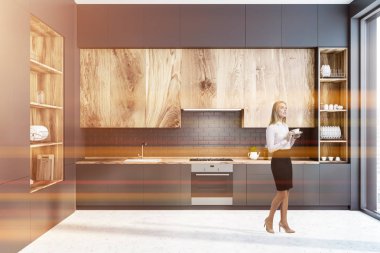 Siyah tuğla duvar, beton zemin, gri mutfak tezgahı ve ahşap dolapları ve soldaki büyük gri ve ahşap dolap modern mutfak iç kadında. Tonlu görüntü