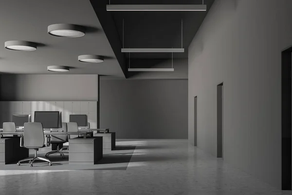 Interior of modern office with gray walls, concrete floor, dark gray computer tables with gray chairs and doors in the wall. 3d rendering