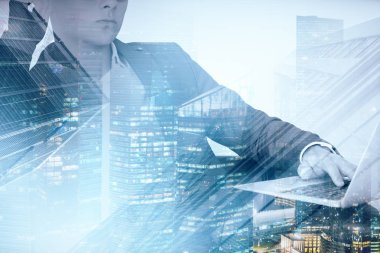 Tanınmayan işadamı koltuk gece cityscape ve gökdelenler çift pozlama ile dizüstü bilgisayar ile oturuyor. Tonlu görüntü