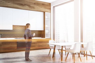 İç siyah tuğla ve beyaz duvarlar, beton zemin, ahşap mutfak tezgahı ve beyaz dolapları ile panoramik mutfak ve beyaz masa sandalye ile bir adam. Tonlu görüntü