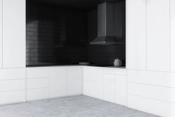 Corner of minimalistic kitchen with black brick walls, concrete floor, white countertops and cupboards and a cooker. 3d rendering