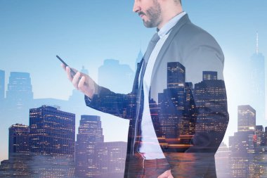 Tanınmayan işadamı smartphone vasıl gece cityscape arka plan üzerinde mavi gökyüzü ile arıyor takım elbiseli. Çift tonlu görüntü pozlaması