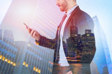 Tanınmayan işadamı smartphone vasıl gece cityscape arka plan üzerinde gökdelenler ile arıyor takım elbiseli. Çift tonlu görüntü pozlaması