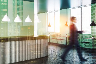 Modern restoran iç yeşil duvarlar, ahşap zemin, gri ve metal resepsiyon masası ve metal sandalye ile ahşap masa ile yürüyen adam. Çift tonlu görüntü pozlaması bulanıklık