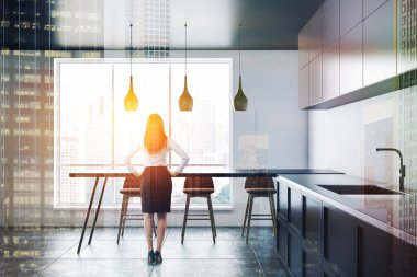 Kadın iç beyaz duvarlar, modern mutfak, lavabo, kahverengi dolap ve masa sandalyeleri yakınındaki pencere ile bar inşa kat, gri mutfak tezgahı ile döşenmiş. Çift tonlu görüntü pozlaması