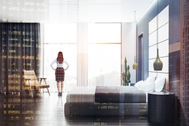 Beyaz ve gri duvarlar, koyu ahşap zemin, geniş pencere, yuvarlak başucu masaları ve deri koltuk gri yatak yatak kadında. Çift tonlu görüntü pozlaması