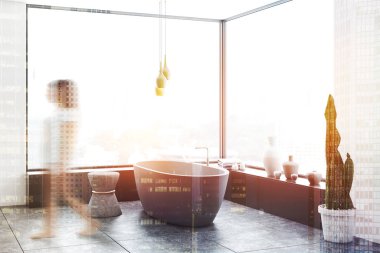 Kadın beyaz duvarlı panoramik banyo köşesinde kat, beyaz küvet duran taş sandalye ve gri çekmeceler yakınındaki döşenir. Çift tonlu görüntü pozlaması bulanıklık