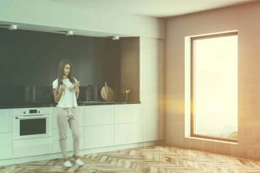 Gri ve siyah mermer duvarlar, ahşap zemin ve yerleşik Ocak ve lavabo ile beyaz mutfak tezgahı ile minimalist çatı katı mutfak kadında. Çift tonlu görüntü pozlaması
