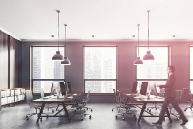 Gri ve koyu ahşap duvarlar, çatı windows, beton zemin ve koyu ahşap bilgisayar tabloları satırları açık alan ofiste iş adamı. Tonlu görüntü