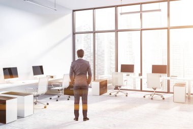 Beyaz duvarları, kiremitli kat, duvar ve pencere ve beyaz sandalye ayakta beyaz ve ahşap Bilgisayar masaları ile panoramik office köşesinde iş adamı. Tonlu görüntü