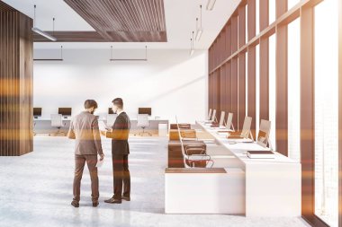 Modern ofis iç beyaz ve ahşap duvarları, kiremitli kat, duvarlar ve beyaz sandalyeler ayakta beyaz ve ahşap bilgisayar tabloları satırları olan iş adamları. Tonlu görüntü