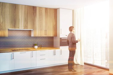 Adam beyaz ve gri duvarlar, ahşap zemin, yapılı içinde fırın ile beyaz mutfak tezgahı ve Ocak ve ahşap dolapları ile mutfak köşesinde. Tonlu görüntü