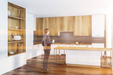 Adam beyaz ve gri duvarlar, ahşap zemin, yapılı içinde lavabo ve fırın, ahşap dolapları ve bar ile beyaz mutfak tezgahı ile mutfak köşesinde. Yapılı içinde ahşap dolap. Tonlu görüntü