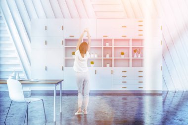 Beyaz duvarlar ile yemek odası iç kadında gri döşeme, ahşap masa beyaz sandalye ve beyaz dolap ayakta duvarın yanında. Tonlu görüntü