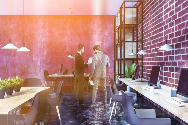 Businessmen in interior of modern office with red and brick walls, long and small wooden computer tables and wooden table with gray chairs. Toned image