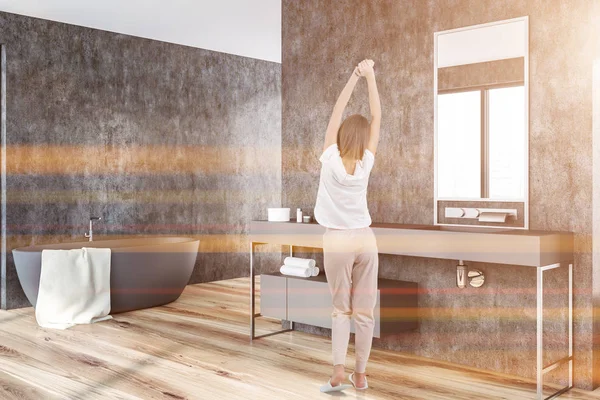 Kadın gri duvarlar, ahşap zemin, bir havlu ile gri küvet banyo köşesinde ve uzun tezgah üzerinde gri lavabo. Tonlu görüntü