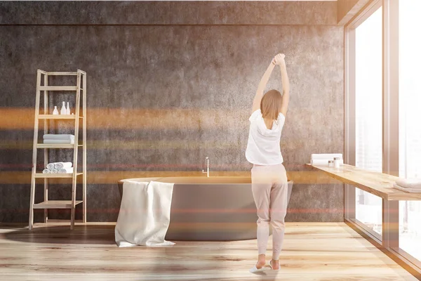 Gri duvarlar, ahşap zemin, üzerine beyaz havlu ile gri küvet ve havlu ve kremler ile ahşap raflar ile şık banyo iç kadında. Büyük pencere. Tonlu görüntü