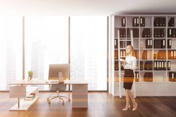 Businesswoman in stylish ceo office interior with white walls, wooden floor, panoramic window, white and wooden computer table and white bookcase with ladder. Toned image