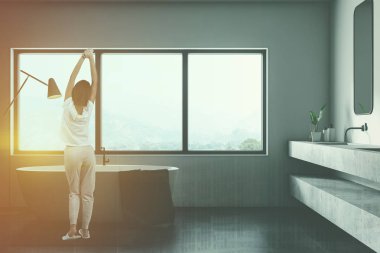 Modern banyo beyaz duvarlı iç kadında, siyah zemin, geniş pencere, beyaz küvet ve beyaz taş çift lavabo dikey ayna ile döşenmiş. Çift tonlu görüntü pozlaması