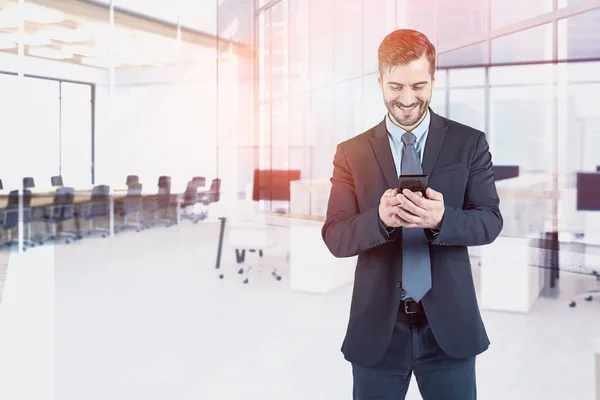 Uomo Affari Barbuto Sorridente Guardando Suo Smartphone Piedi Ufficio Moderno — Foto Stock