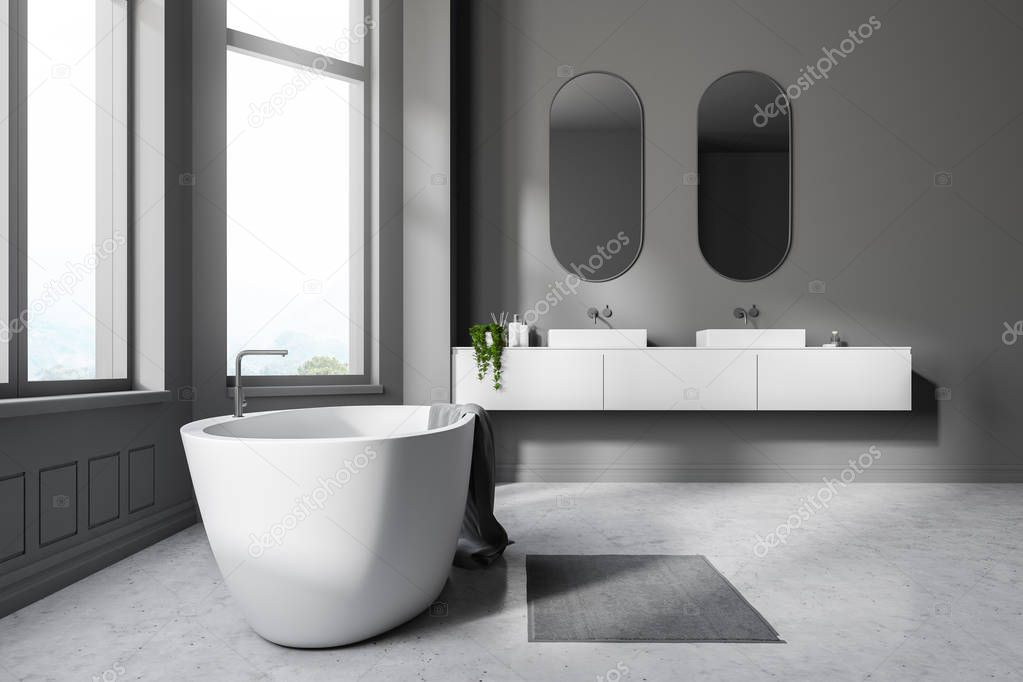 Interior of modern bathroom with gray walls, concrete floor, white bathtub with a towel on it and two white sinks on white counter with oblong mirrors above them. 3d rendering