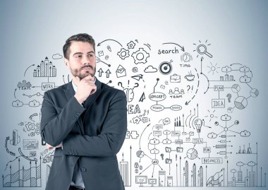 Koyu takım elbise ayakta iş planı kroki ile gri duvarının yakınında üzerinde giyiyor sakallı dalgın Genç beyaz işadamı portresi